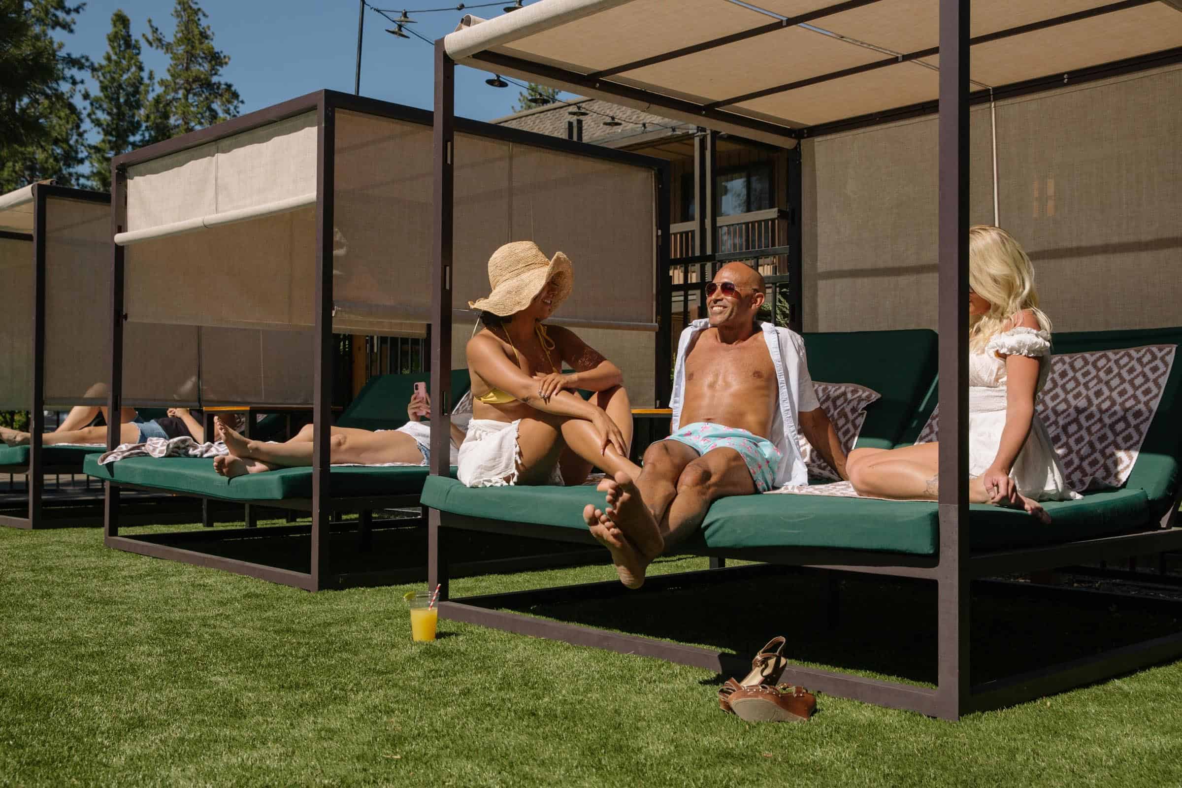 A group of people relaxing on lounge chairs with canopies in a grassy area.